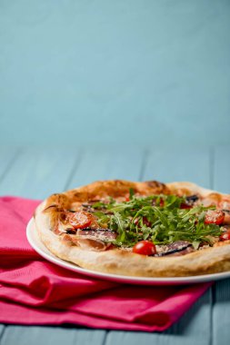 Christmas pizza on the wood board. Holiday celebration pizza with prosciutto crudo and cherry tomatoes over blue background. Copy space banner. Italian cuisine concept.