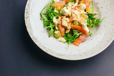 Salata - sebzeli ve üzümlü füme somon. Lezzetli eşsiz tarif, akşam yemeği için sağlıklı salata. Siyah arkaplanda servis edilen.