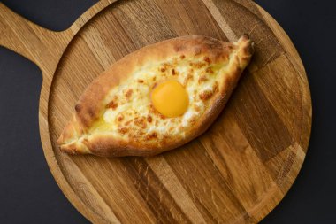 Khachapuri with cheese and egg on a wooden board over black background. Georgian cuisine concept. Close up.