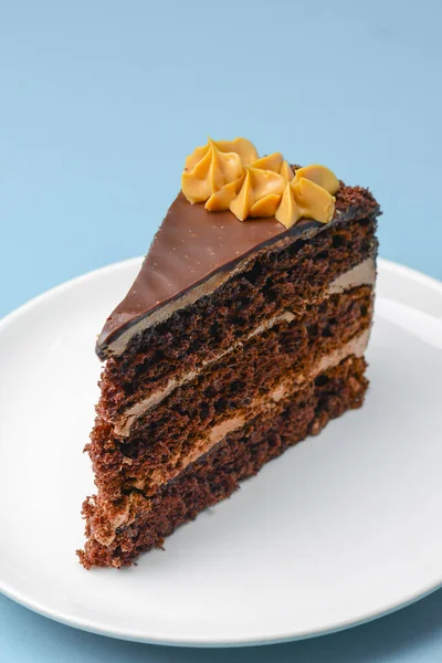 Piece of chocolate cake with icing on blue background. Sweet dessert for tea or coffee time. Close up.