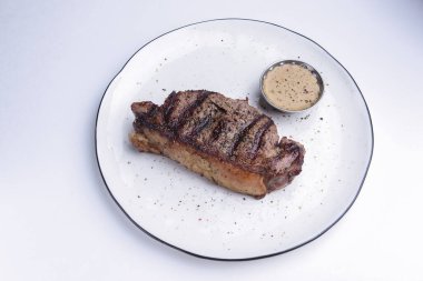 Beyaz arka planda beyaz bir tabakta servis edilen soslu leziz biftek. Barbekü eti, barbekü konsepti. Lezzetli yemek fikri..