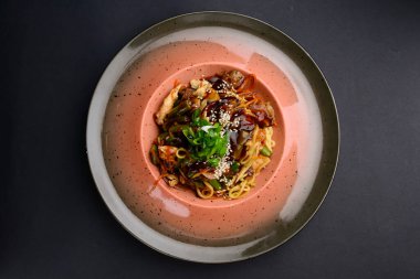 Asian wok with stir fry chicken and vegetables, wok salad in white ceramic plate served over black background. Asian cuisine concept, eating out.