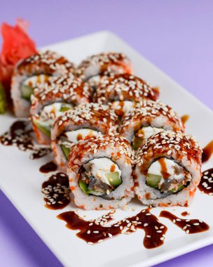 Yılanbalığı ve unagi soslu Japon suşisi seti. İçinde krem peynir var. Pastel renkli mor arka planda beyaz bir tabakta servis edilmiş. Geleneksel tarif.