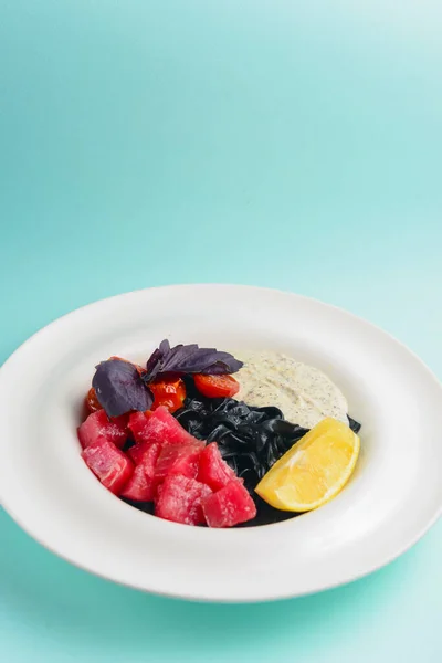 Assiette avec pâtes maison noires au saumon salé, servie sur une table de fond bleue. — Photo