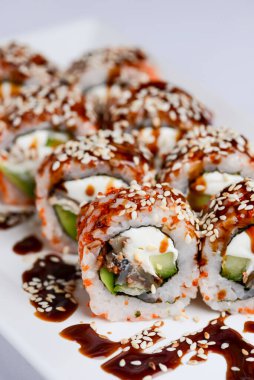 Yılanbalığı ve unagi soslu Japon suşisi seti. İçinde krem peynir var. Beyaz arka planda beyaz bir tabakta servis edilmiş. Geleneksel tarif.