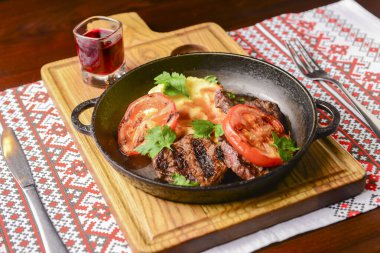 Geleneksel Ukrayna masa örtüsünün üzerinde ızgara domatesli bir tavada servis edilen sulu biftek. Ukrayna mutfağı kavramı, barbekü kavramı.