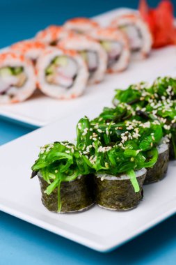 Maki Suşi, füme somon ve krem peynirden yapılmış rulo. Geleneksel Japon mutfağı konsepti, mavi arka planda. Geleneksel tarif.