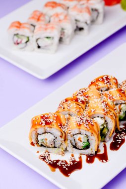 Mor arka planda beyaz bir tabakta sunulan unagi soslu yılan balığı, somon balığı ve ton balığı. Geleneksel Japon mutfağı, Asya mutfağı kavramı.