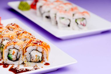 Mor arka planda beyaz bir tabakta sunulan unagi soslu yılan balığı, somon balığı ve ton balığı. Geleneksel Japon mutfağı, Asya mutfağı kavramı.