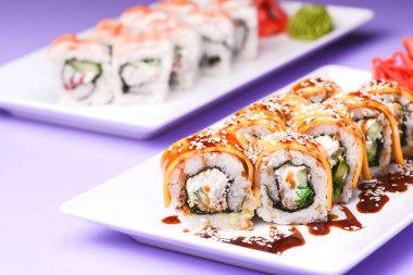 Mor arka planda beyaz bir tabakta sunulan unagi soslu yılan balığı, somon balığı ve ton balığı. Geleneksel Japon mutfağı, Asya mutfağı kavramı.