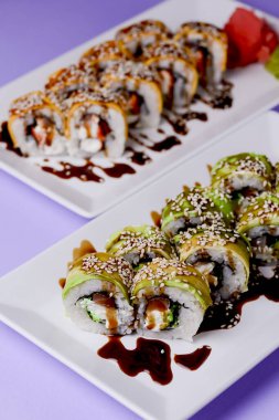 Mor arka planda beyaz bir tabakta sunulan unagi soslu yılan balığı, somon balığı ve ton balığı. Geleneksel Japon mutfağı, Asya mutfağı kavramı.