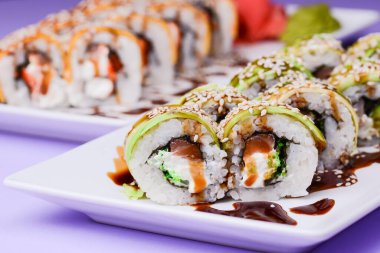 Mor arka planda beyaz bir tabakta sunulan unagi soslu yılan balığı, somon balığı ve ton balığı. Geleneksel Japon mutfağı, Asya mutfağı kavramı.