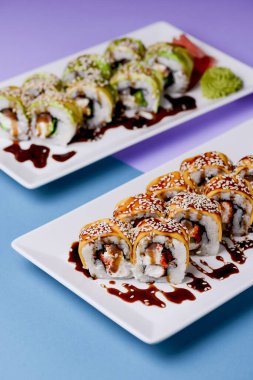 Mor arka planda beyaz bir tabakta sunulan unagi soslu yılan balığı, somon balığı ve ton balığı. Geleneksel Japon mutfağı, Asya mutfağı kavramı.