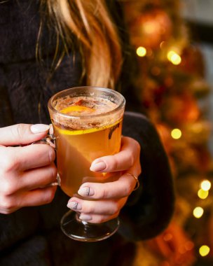 Kadın ellerinde sıcak şarap, arka planda Noel süslemeleri, yeni yıl zamanı. Soğuk hava için sıcak içecek.