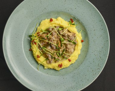 Üzerinde mantar sosu olan zengin ve lezzetli patates püresi siyah arka planda mavi bir tabakta servis edilir. Kapat..