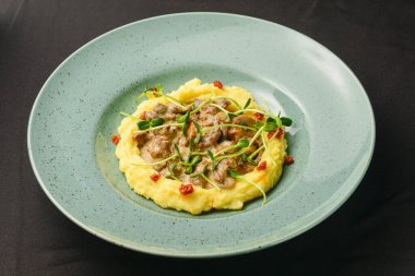 Üzerinde mantar sosu olan zengin ve lezzetli patates püresi siyah arka planda mavi bir tabakta servis edilir. Kapat..