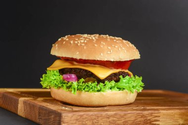 Kırmızı soğanlı pastırma ve köfteli burger ve siyah arka planda peynir. Fast food, abur cubur konsepti. Köy tahtasında sulu bir burger.