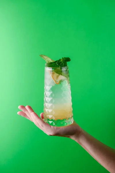 明るい緑の背景の上に手でミントで飾られています アルコール飲料 パーティーで飲む楽しいカクテル 緑に隔離された — ストック写真