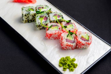 Suşi seti, krem peynirli suşi ruloları ve siyah arka planda beyaz bir tabakta servis edilen havyar. Geleneksel Japon mutfağı kavramı.