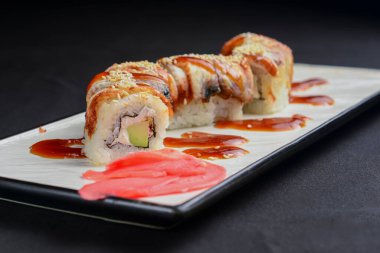 Suşi seti, krem peynirli suşi ruloları ve siyah arka planda beyaz bir tabakta servis edilen yılan balığı. Geleneksel Japon mutfağı kavramı.