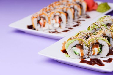 Maki suşi rulosu füme yılan balığı, krem peynir ve unagi sosundan yapılır. Geleneksel Japon mutfağı kavramı. Mor arka planda beyaz bir tabakta servis edilmiş..