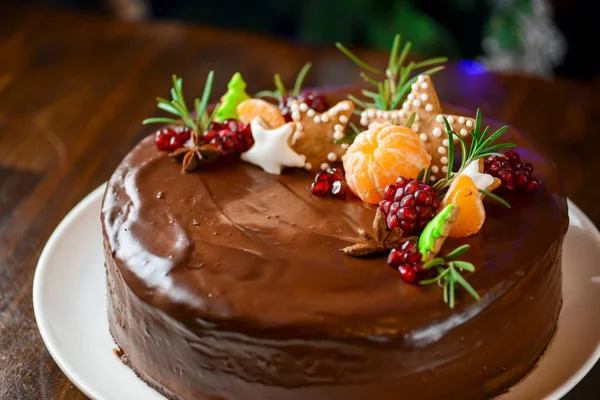 Nar tohumları ve mandalinayla süslenmiş Noel çikolatalı pasta. Yeni yıl kutlaması için pasta, Noel partisi. Arka planda Noel ağacı.