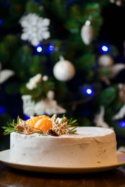 Kış Noel süslü Noel pastası, arka planda Noel ağacı. Üstünde mandalina olan çikolatalı vanilyalı pasta. 2021 Yeni Yıl Kutlaması.