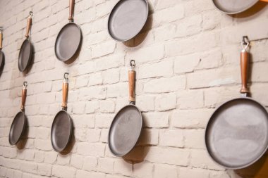 Kızartma tavaları beyaz tuğla duvara dayanıyor. Beyaz arka planda boş tavalar. Dokulu duvar afişi. Mutfak aletleri..