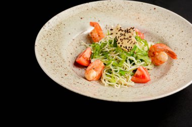 Siyah arka planda seramik tabakta servis edilen karidesli yeşil salata. Lezzetli salata, karides ve taze sebze..