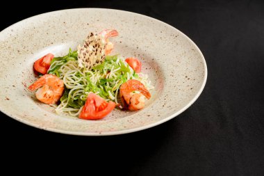 Siyah arka planda seramik tabakta servis edilen karidesli yeşil salata. Lezzetli salata, karides ve taze sebze..