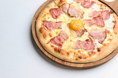 Beyaz arka planda tahta bir tahtada servis edilen domuz pastırmalı ve yumurta sarısı tavuklu pizza. İtalyan mutfağı kavramı..