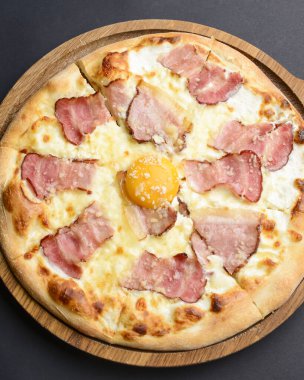 Domuz pastırmalı pizza carbonara ve siyah arka planda tahtanın üzerinde servis edilen tavuk yumurtası sarısı. İtalyan mutfağı kavramı..