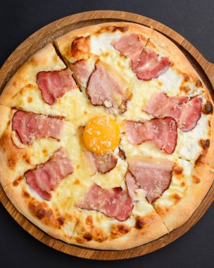 Domuz pastırmalı pizza carbonara ve siyah arka planda tahtanın üzerinde servis edilen tavuk yumurtası sarısı. İtalyan mutfağı kavramı..