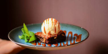 Bulanık arka planda mavi bir tabakta servis edilen dondurmalı bozulmuş browni. Lezzetli Amerikan tatlısı, geleneksel tarif..