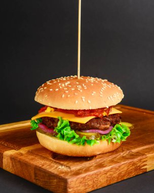 Kırmızı soğanlı pastırma ve köfteli burger ve siyah arka planda peynir. Fast food, abur cubur konsepti. Köy tahtasında sulu bir burger.