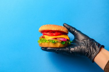 Ev yapımı ızgara hamburger ve parlak mavi arka planda siyah eldiven. Uzay afişini kopyala. Abur cubur, fast food konsepti.