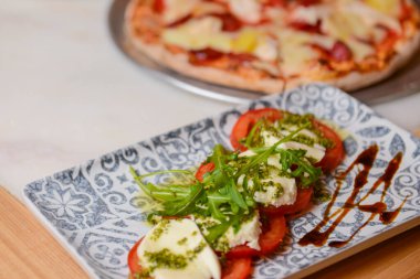Klasik caprese salatası ve pizza. Arka planda bulanık bir fotoğraf. Geleneksel İtalyan mutfağı kavramı. Caprese salatasına odaklan..