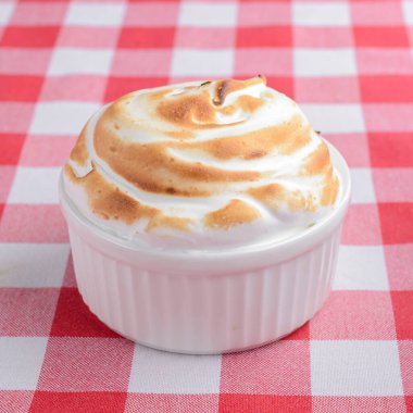 Creme Brulee 'nin tatlısını. Üstünde krem şanti olan küçük bardakta vanilyalı tatlı. Kırmızı ekose masa örtüsünün üstünde..