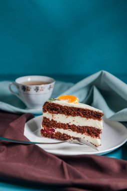 Vanilyalı çikolatalı kek. İçinde böğürtlen ve üstünde bir parça mandalina var. Renkli mavi arka planda beyaz bir tabakta servis edilmiş. Kahve ya da çay saati için tatlı..