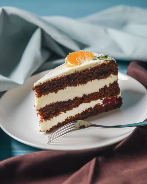 Vanilyalı çikolatalı kek. İçinde böğürtlen ve üstünde bir parça mandalina var. Renkli mavi arka planda beyaz bir tabakta servis edilmiş. Kahve ya da çay saati için tatlı..