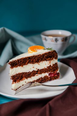 Vanilyalı çikolatalı kek. İçinde böğürtlen ve üstünde bir parça mandalina var. Renkli mavi arka planda beyaz bir tabakta servis edilmiş. Kahve ya da çay saati için tatlı..