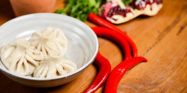 Khinkali seramik bir tabakta pişirildi. Nar, kırmızı biber ve arka planda taze yeşillik. Kırsal ahşap masa. Etli börek, Gürcü mutfağı konsepti.