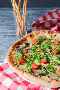 Prosciutto ve Arugula Pizza ve kiraz domatesli ekmek çubuklarıyla kırmızı ekose masa örtüsünün üzerinde beyaz bir tabakta servis ediliyor. İtalyan mutfağı, geleneksel pizza tarifi..