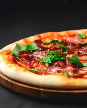 Siyah arka planda taze lezzetli pizza. Siyah üzerine kızarmış sosis ve roka ile geleneksel İtalyan pizzası. İtalyan mutfağı kavramı.