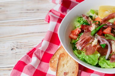 Prosciutto ve roka salatası ahşap arka planda beyaz bir kasede. Kırmızı ekose masa örtüsü. İtalyan mutfağı kavramı, sebzeli sağlıklı yemek salatası..