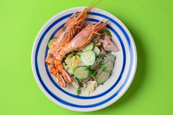 A healthy green garden salad with cooked shrimps over green background. Delicious dinner idea, healthy food, sea food. Top view, flat lay.