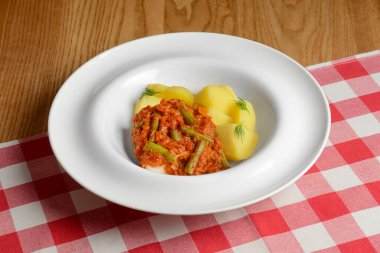 Üzerine sos dökülmüş haşlanmış patates. Kırmızı ekose masa örtüsünün üzerinde beyaz bir tabakta servis edilmiş. Ukrayna ve Rus mutfağı kavramı.