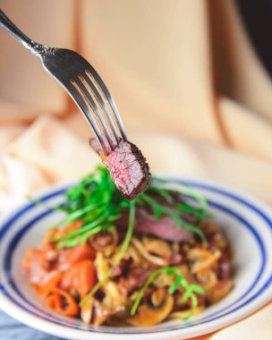 Yumurtalı makarna, sığır eti, mantar ve taze biberiye ve roka ile süslenmiş kremalı makarna. Masa örtüsüyle ahşap arka planda beyaz bir tabakta servis edilmiş. İtalyan mutfağı kavramı.