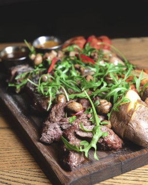 Restoranda ya da barda ahşap bir tahtada servis edilen taze roka ile kaplı kızarmış et ve sebzeler. Abur cubur, fast food konsepti, dışarıda yemek..