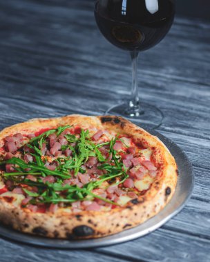 Somon balığı, peynir ve roka ile pizza ve kırsal gri ahşap arka planda bir bardak kırmızı şarap. İtalyan mutfağı konsepti, geleneksel pizza tarifi.